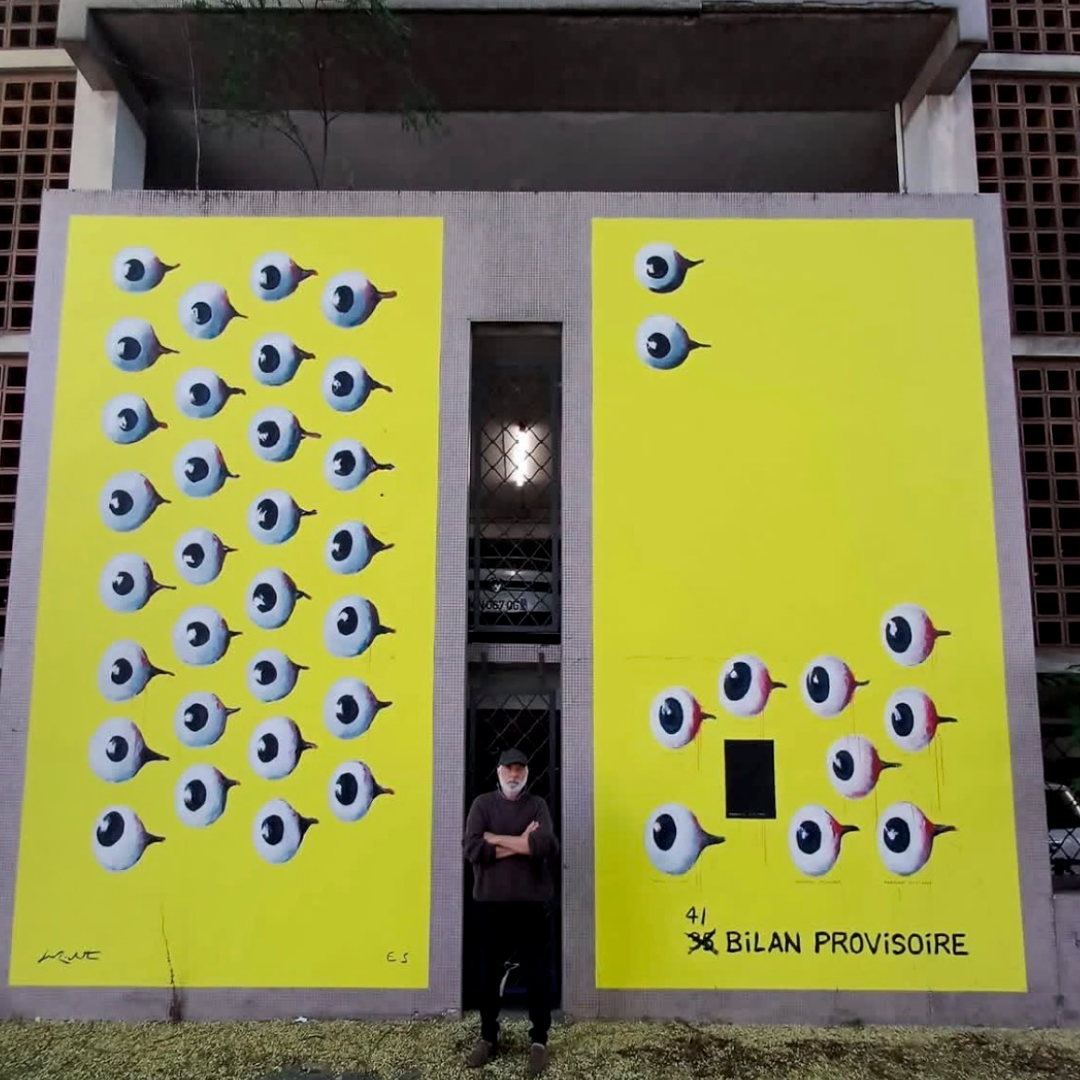 Artwork 1: Bilan provisoire, a mural of eyes on two yellow walls, with Jean-Marc Rochette standing between them.
