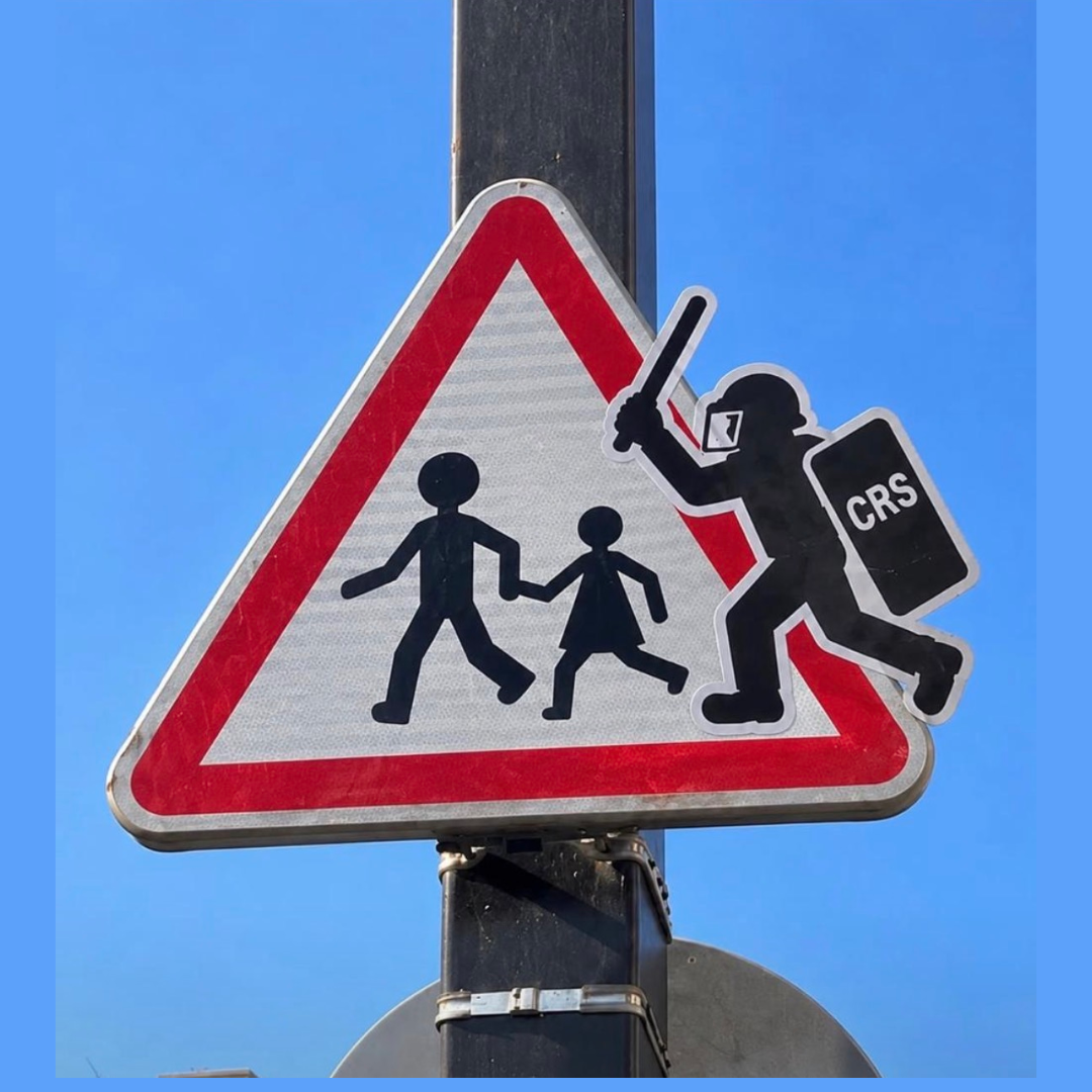 Artwork 4: A school-crossing road sign altered to show a CRS officer approaching two children with a baton.