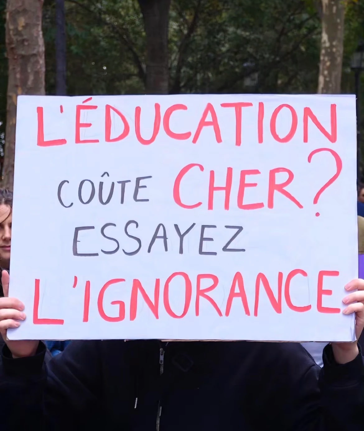 Protest sign reading: L’ÉDUCATION COÛTE CHER ? ESSAYEZ L’IGNORANCE