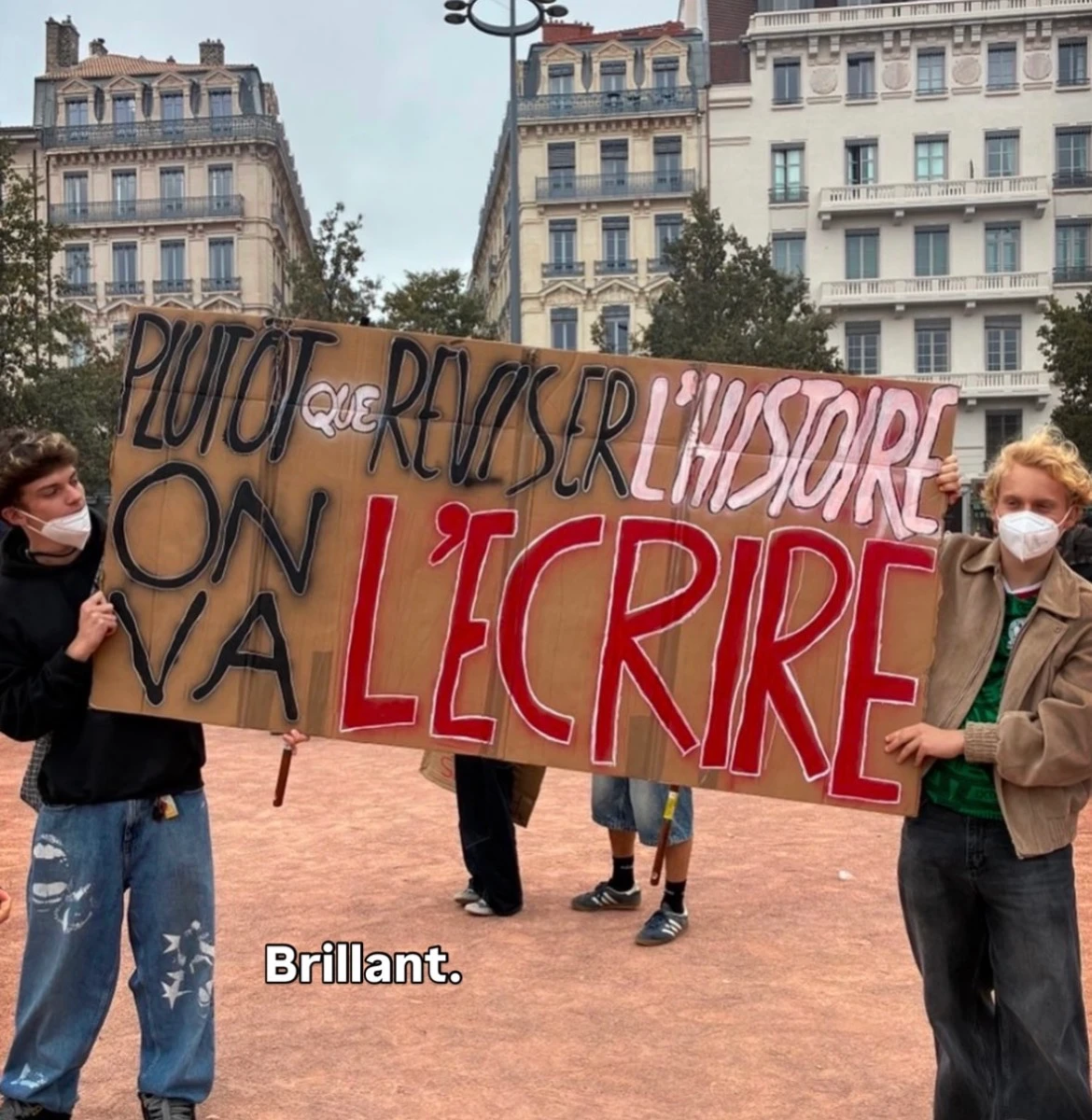 Protest sign reading: PLUTÔT QUE RÉVISER L’HISTOIRE ON VA L’ÉCRIRE